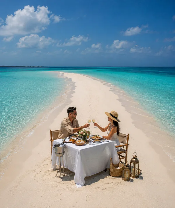Couple portant un toast à une table dressée sur un banc de sable au milieu du lagon turquoise