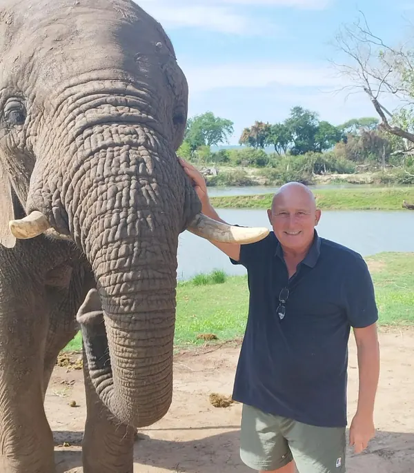 Patrick aux côtés d'un éléphant aux longues défenses, près d'un fleuve