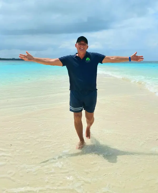 Patrick sur une plage de Zanzibar, bras ouverts dans l'eau turquoise