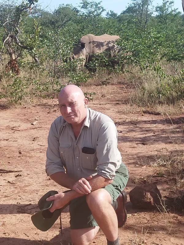 Patrick assis dans la brousse, un rhinocéros derrière lui au Zimbabwe