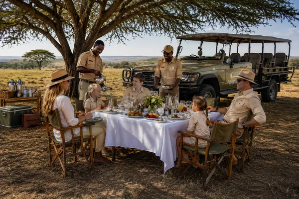 Famille attablée pour un petit-déjeuner servi en pleine savane, guides aux petits soins